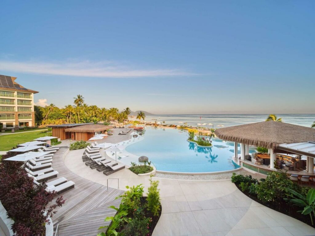 Big pool area with lounge chairs and a bar with the ocean in the distance at Hilton Hotel Tahiti.