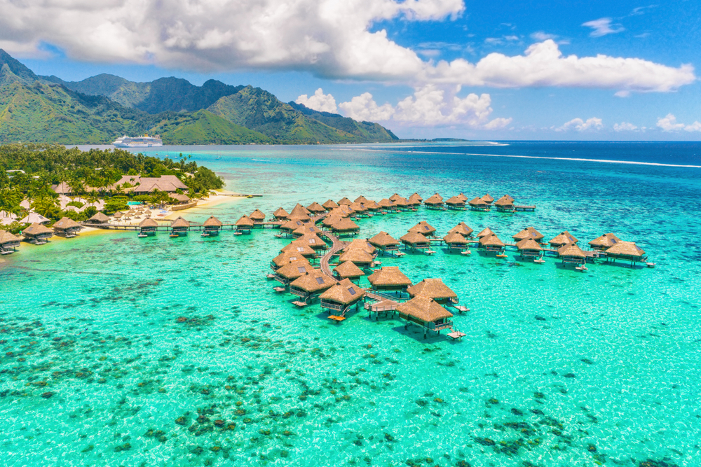Aerial view of bungalows over clear, turquoise water on a sunny day in Bora Bora.