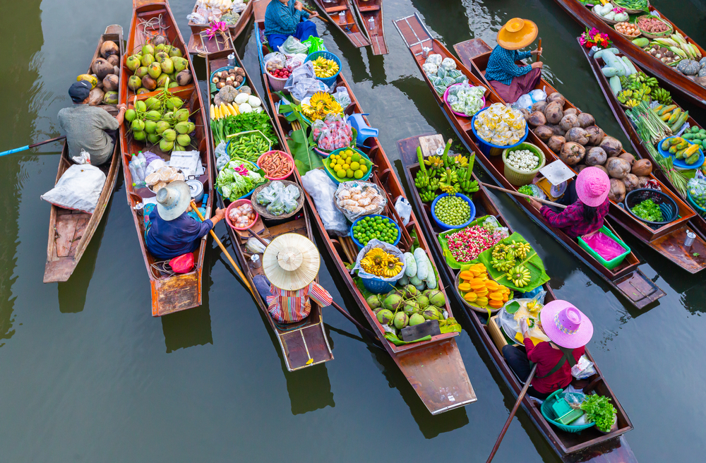 View looking down at boats piled with fresh fruit with people paddling.
