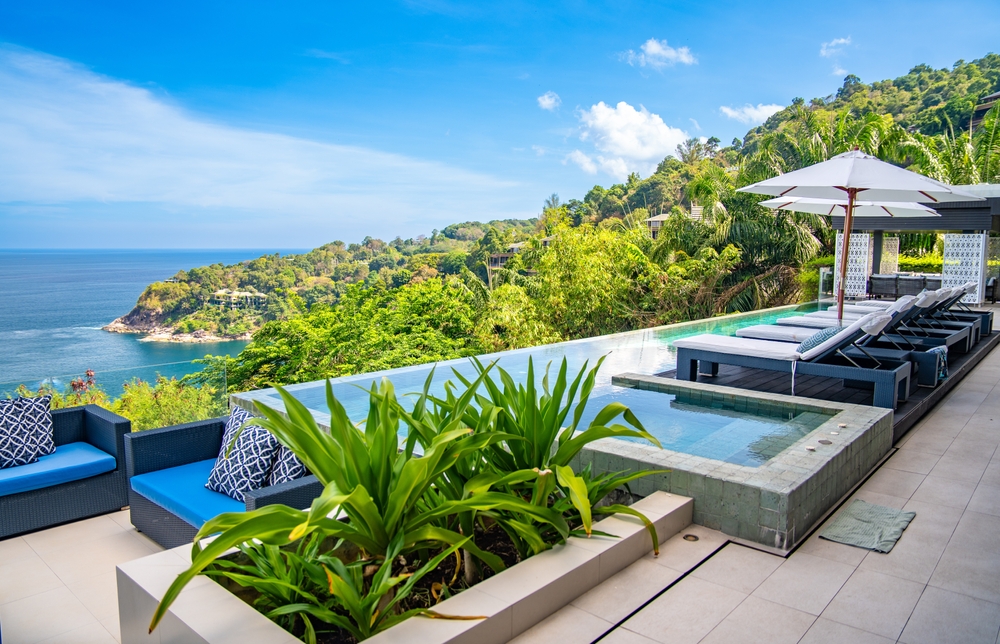 A resort pool area with lounge chairs overlooking the ocean and jungle in Thailand.