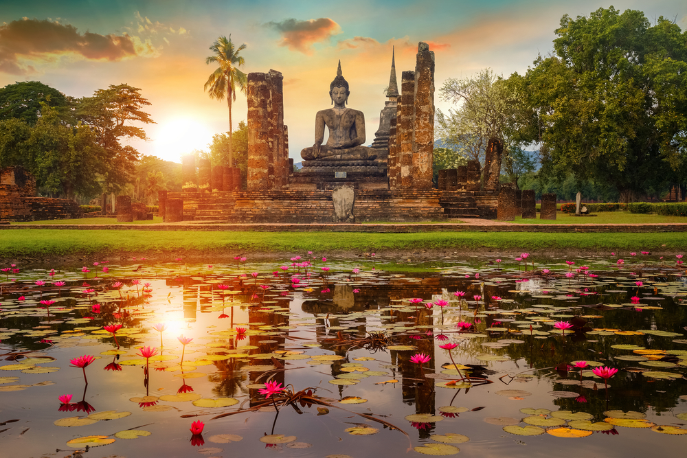 Golden hour at Wat Mahathat Temple featuring a statue and pond with lily pads.