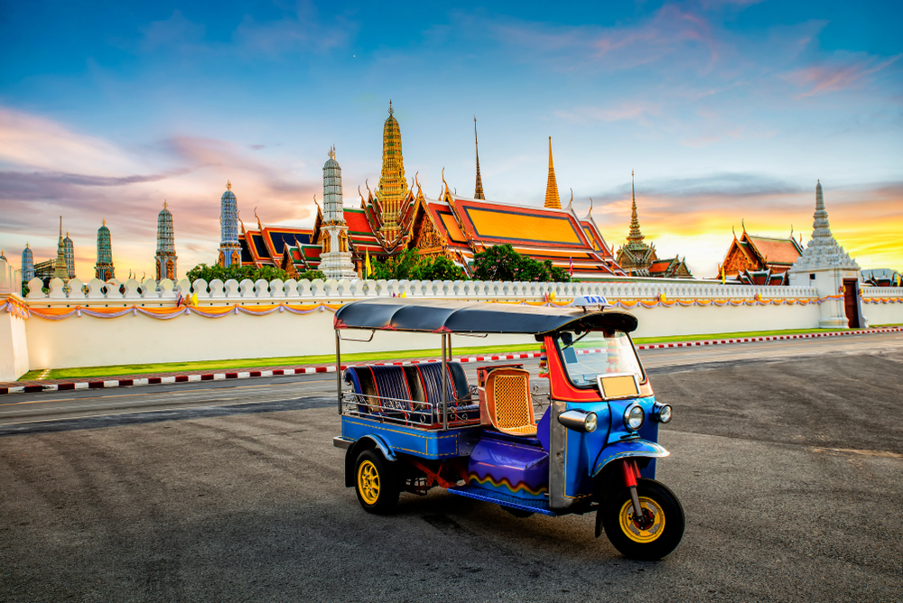 An empty, blue tuk tuk sitting in front of a temple in Thailand.