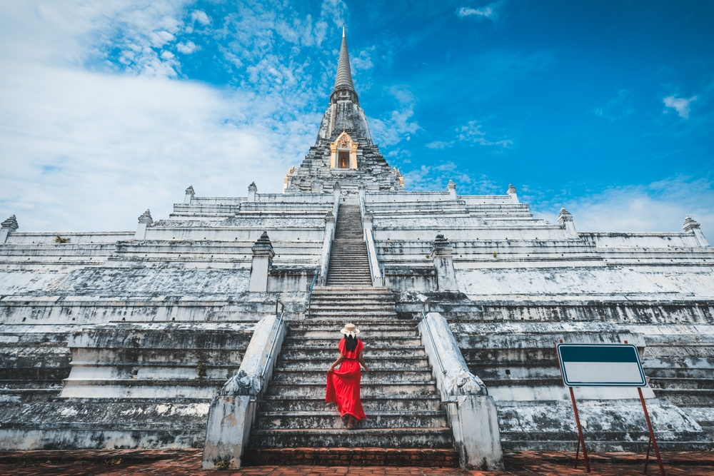 Woman in a long red dress and a hat walking up many stairs at Wat Phu Khao Thong temple.