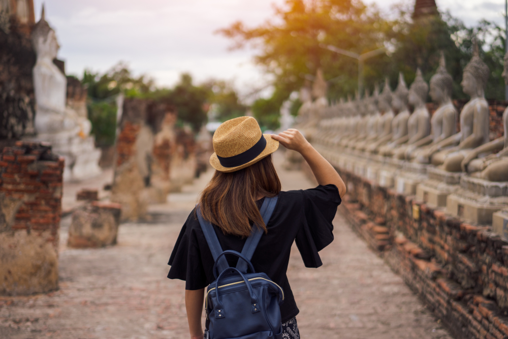 Woman wearing a black shirt, backpack, and hat walks through Wat Yai Chai Mongkol while traveling to Thailand.