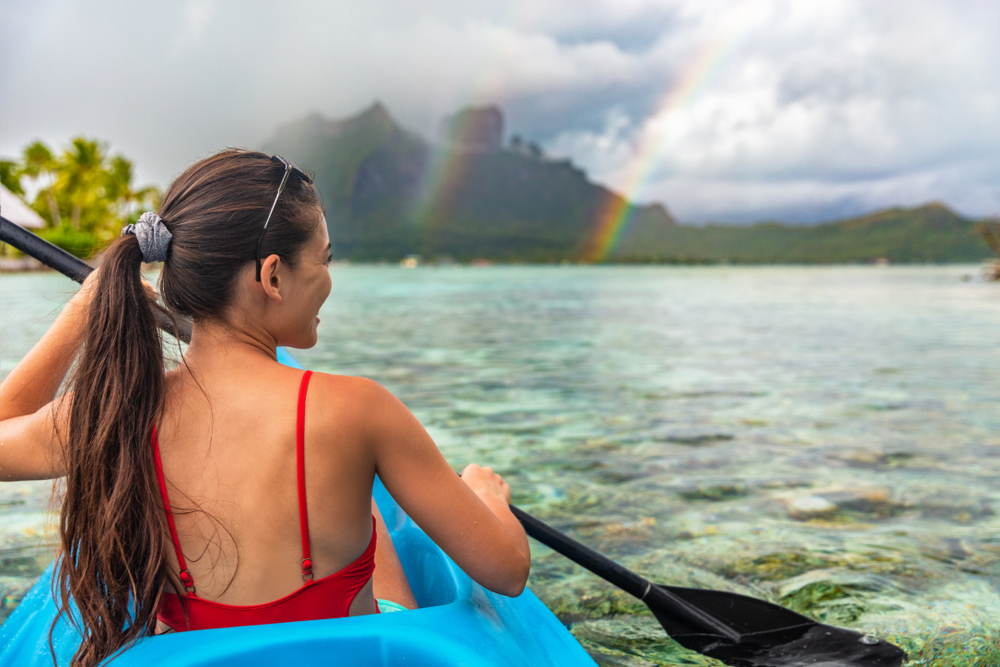 Woman kayaking in the ocean with a double rainbow in the background.