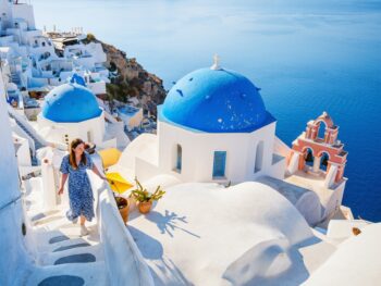 girl walking the white steps with white buildings and blue domes beside it the greek islands