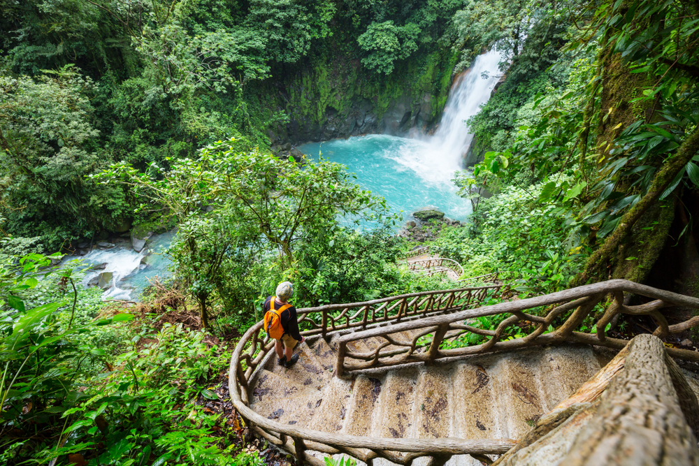 Majestic waterfall in the rainforest jungle of Costa Rica. Tropical hike. A woman hiker is stood half way up the stairs.