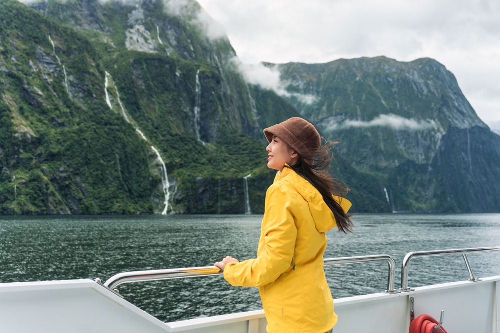 Young,Asian,Woman,Enjoying,The,View,Of,Milford,Sound,During Young asian woman enjoying the view during cruise. Article is about Disney Cruise Outfits for August