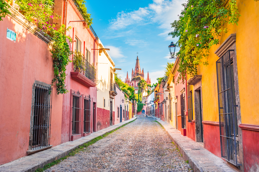 Beautiful cobblestoned street and colorful facades of city with pink castle spires in distance.