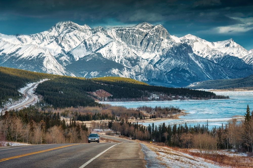 view of a road on a highway with snow mountains in the backdrop