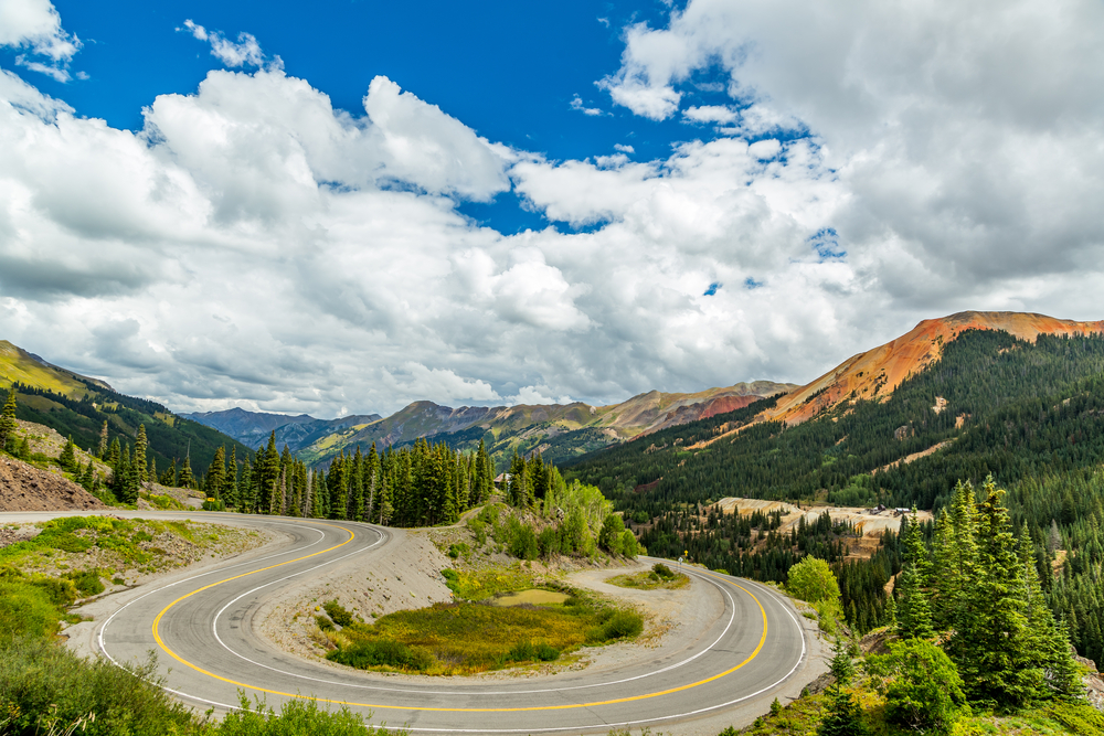 San Juan National Forest, Colorado showing the road with a sharp bend and mountains. The article is about a Colorado road trip.