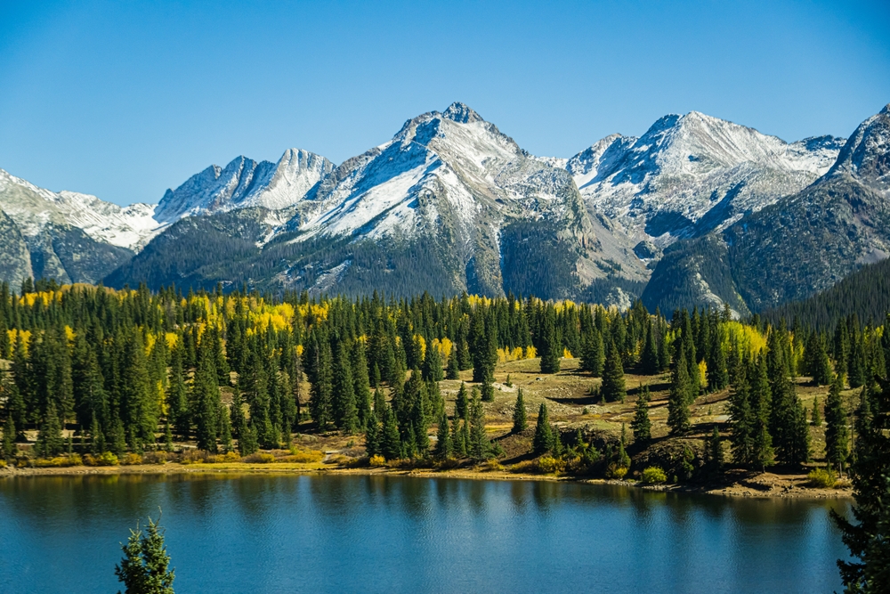 Colorado Rocky Mountains in the Fall with snow capped mountains in the background. There is a lake in the foreground. 