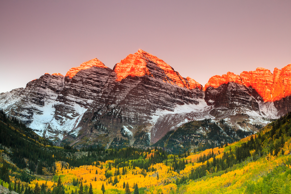 sunrise hitting the mountains and turning them orange in Colorado. The article is about a Colorado road trip.