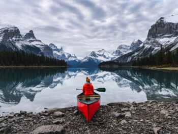 traveler sitting with paddle on canoe in front of a lake reflecting mountains things to do in jasper