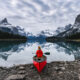 traveler sitting with paddle on canoe in front of a lake reflecting mountains things to do in jasper