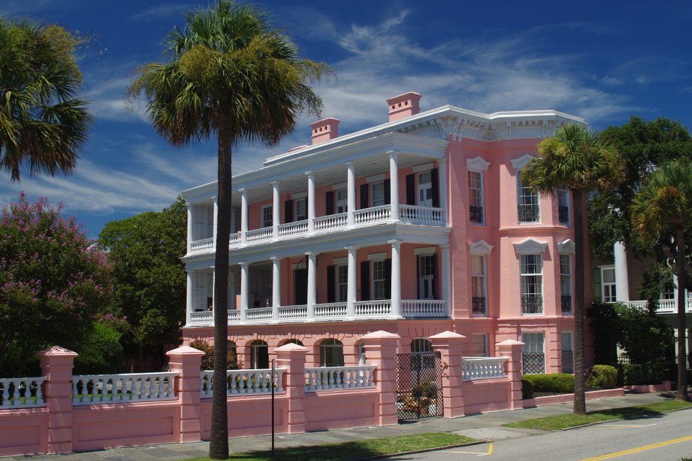 Pink house on a street with palm trees. The article is a Charleston Travel Guide.