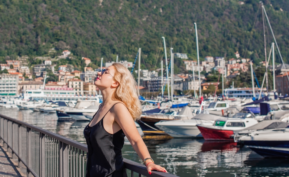 Blonde Caucasian woman leaning against railing, marina boats in background