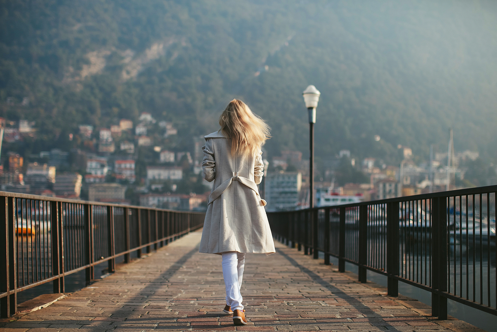 blonde girl stands with her back on the waterfront mountain 
