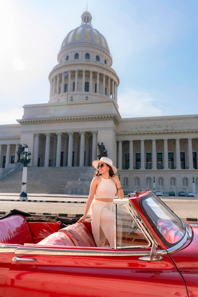 Woman stood up in classic 50's car. The article is about traveling to Cuba.
