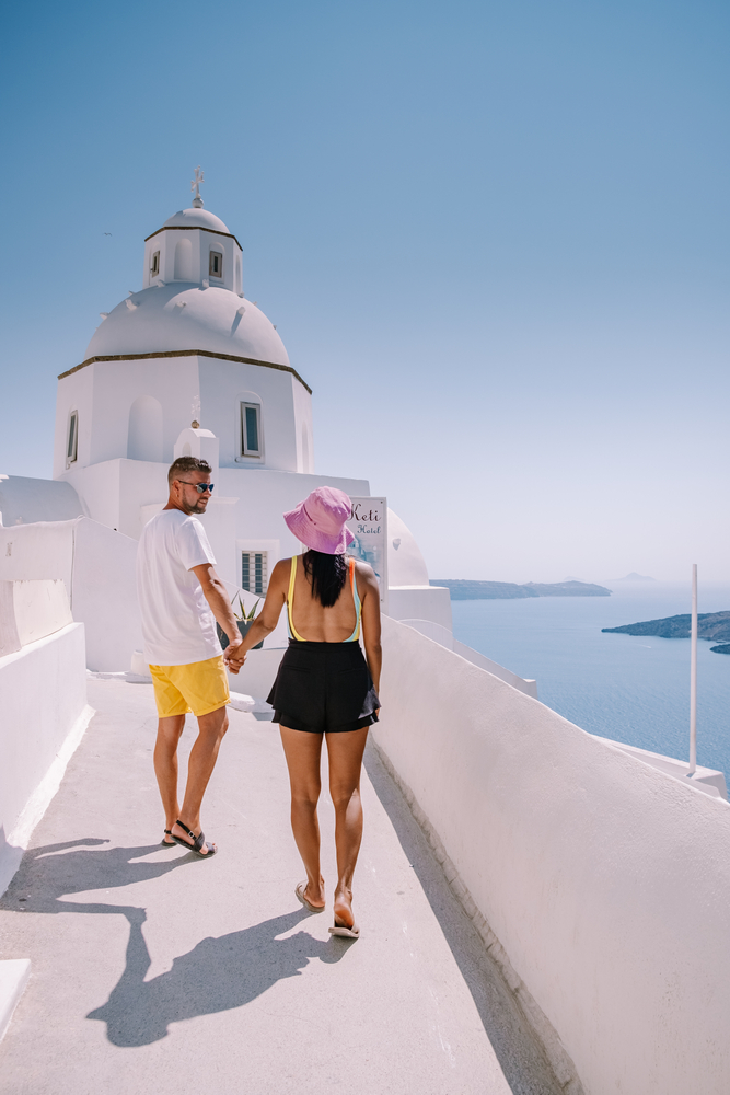 young couple on luxury vacation at the Island of Santorini watching sunrise by the blue dome church and whitewashed village of Oia Santorini Greece.