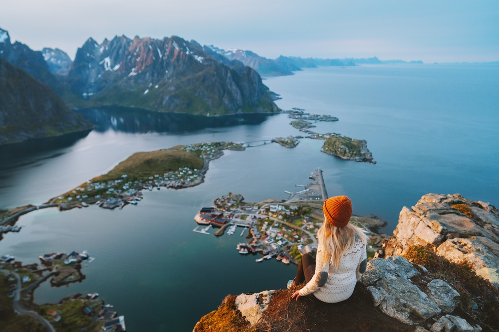 woman sitting on the edge of a cliff looking at the mountains and islands traveling to norway