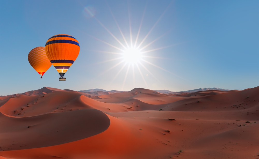 hot air balloon flying over sand dunes traveling to morocco