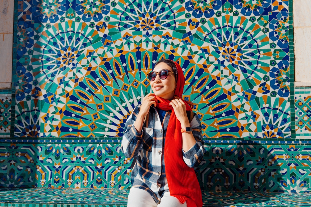 woman wearing a scarf and sunglasses in front of a colorful mosaic wall