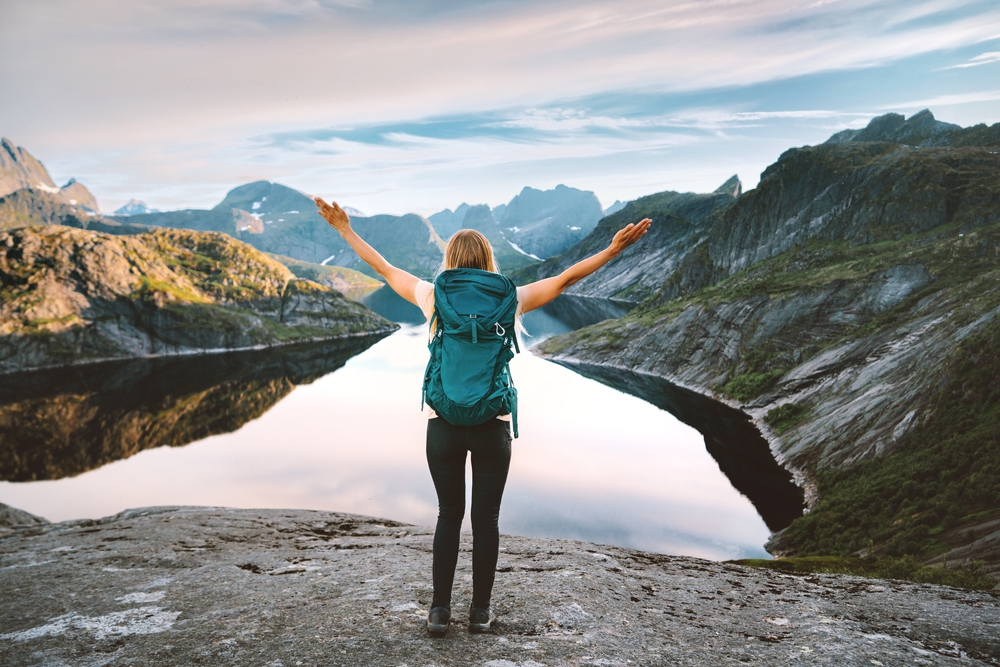 woman with a backpack standing in front of a lake and mountains