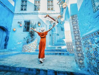 girl in orange dress standing in a blue house area traveling to morocco