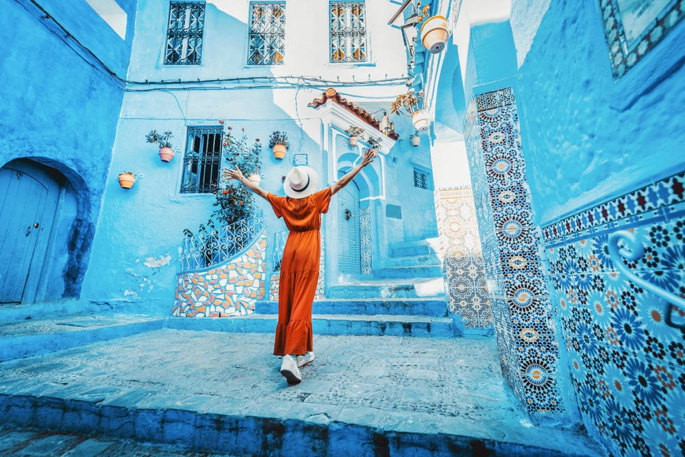 girl in orange dress standing in a blue house area traveling to morocco