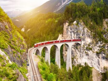 red train on viaduct in mountain european train trips