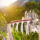 red train on viaduct in mountain european train trips