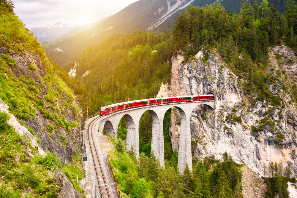 red train on viaduct in mountain european train trips