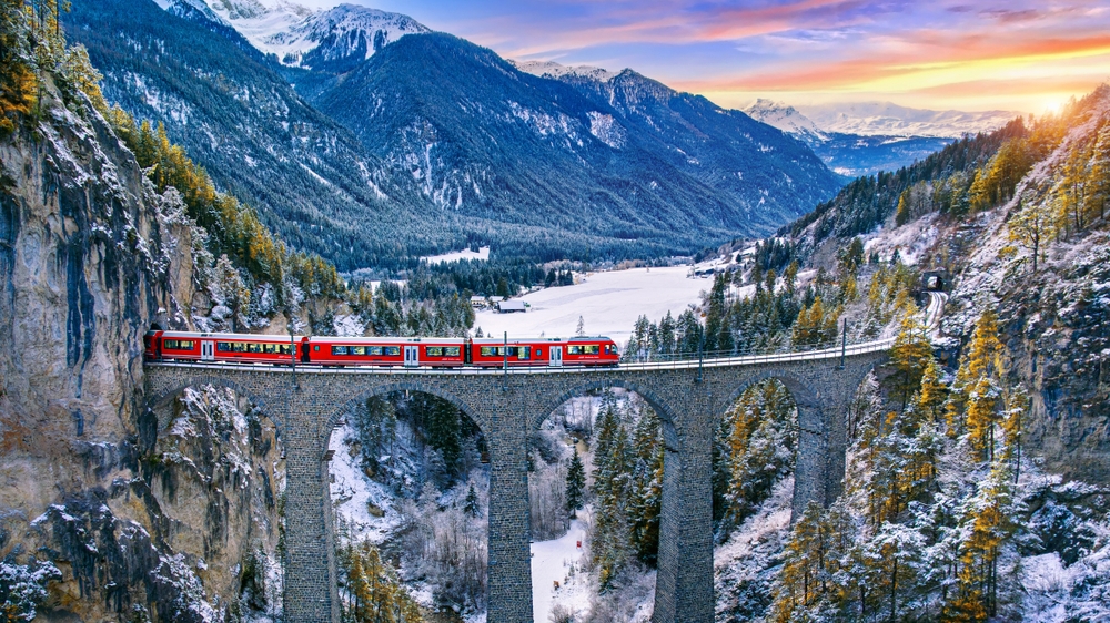 aerial view of red and white colored train passing through a viaduct european train trips