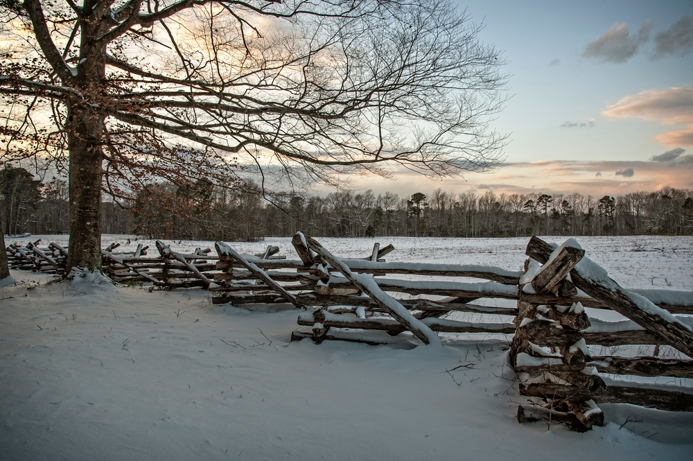 Surrender Field in Yorktown, Virginia, this picture captures a serene winter landscape featuring a rustic wooden split-rail fence covered in snow.