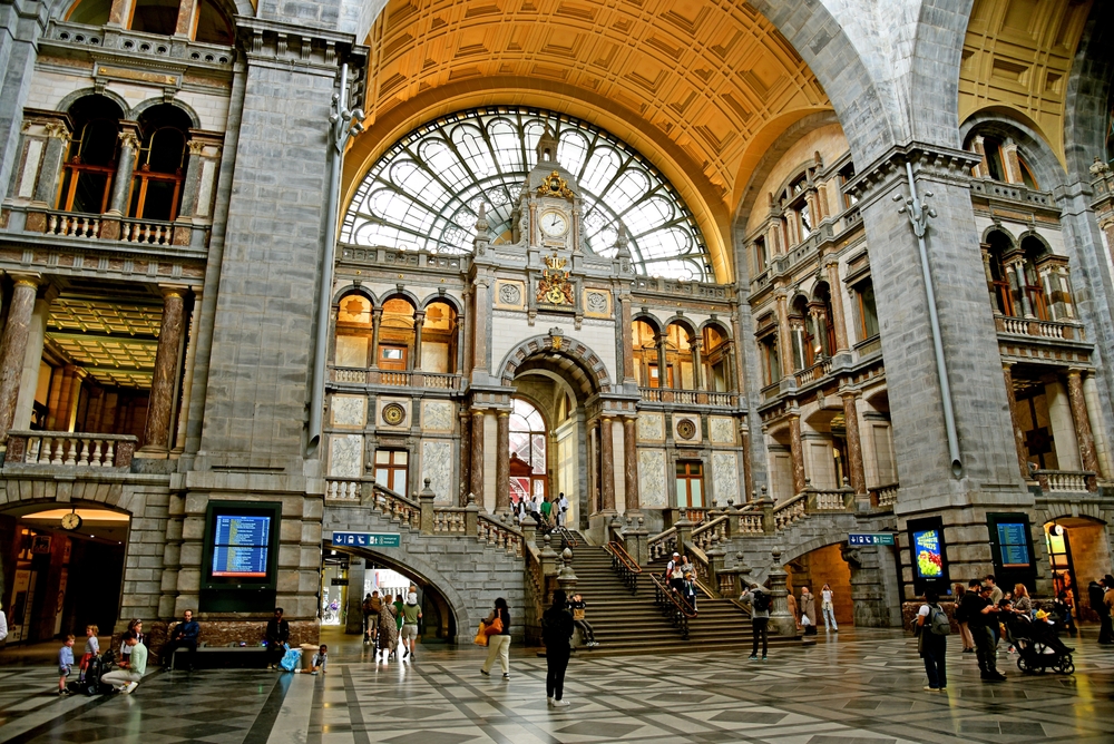 Antwerp Central Train Station. It is ornate with arches and balconies. There are people in the station.