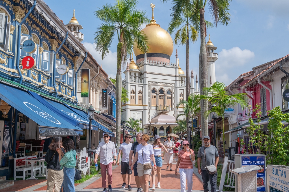 Causasian people walking away from mosque with golden dome. Colorful shops on right and left.