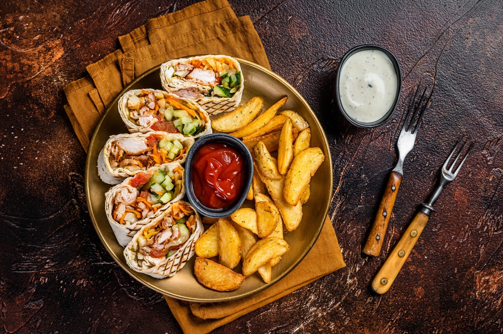 Chicken shawarma durum doner kebab with vegetable salad and french fries. Dark background. Top view.