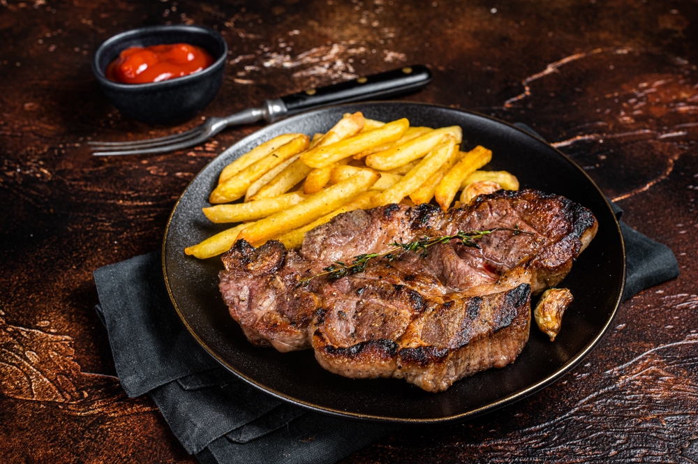 Roasted  steaks from on plate with potato chips. Dark background. Top view. The article is about best restaurants in Philadelphia. 
