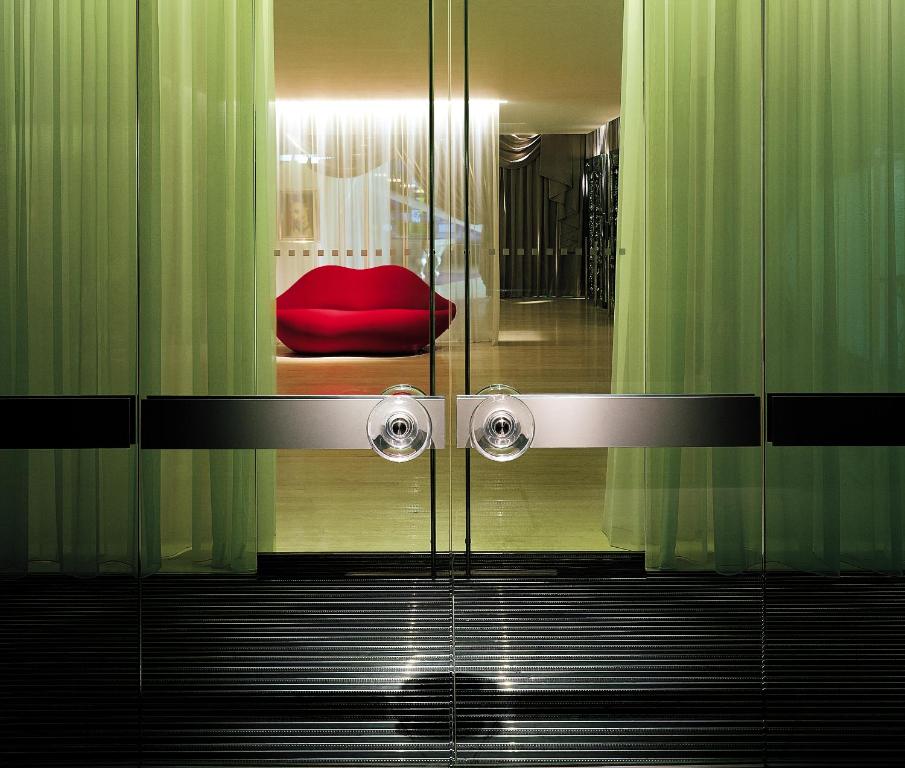 Doors to hotel with red lip sofa beyond. you can see glass walls and draped material.  The article is on  best boutique hotels in London. 