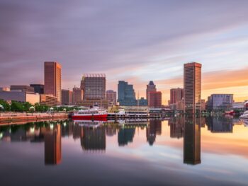 buildings reflecting in the water during sunset traveling to Baltimore