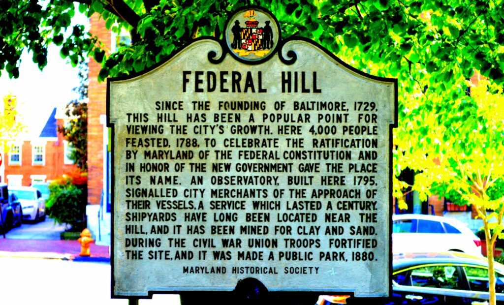 The article is about a Baltimore weekend getaway. an historical sign from the Maryland Historical Society relates the history of Federal Hill, which later grew into a prominent neighborhood in the city.